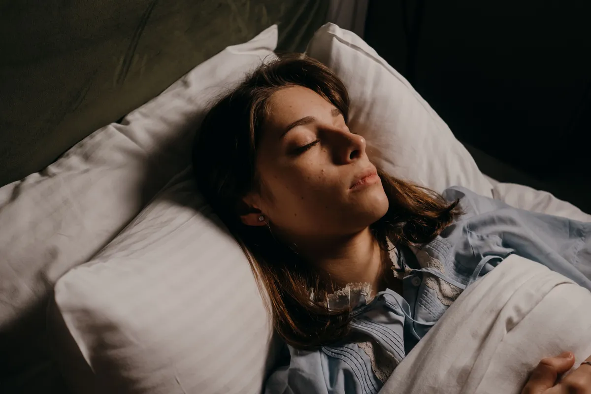 A woman asleep on her back in bed at night in warm low light.