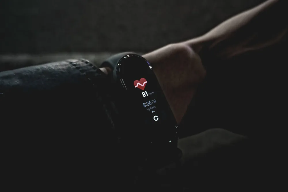 A fitness tracker glowing on a wrist in a dark bedroom at night, showing a heart-rate reading.