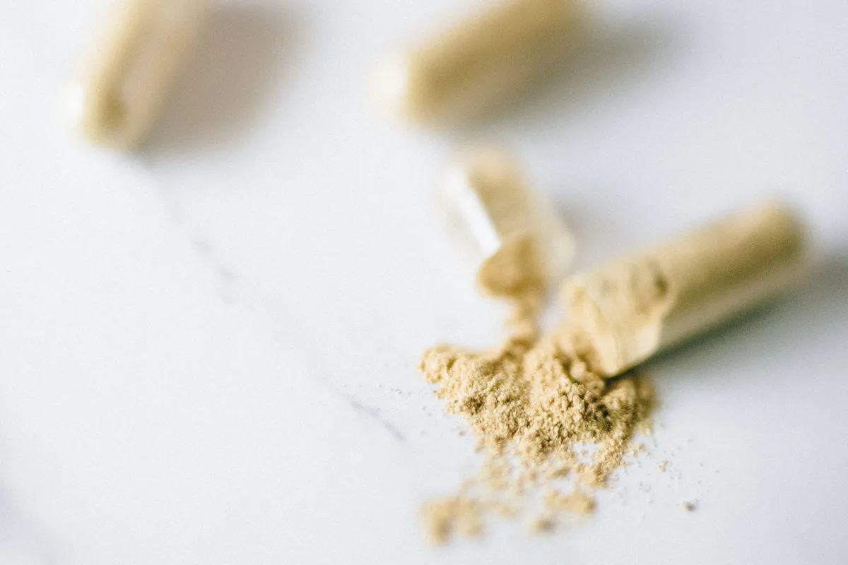 Ashwagandha supplement capsules and a spill of tan root powder on a light surface.