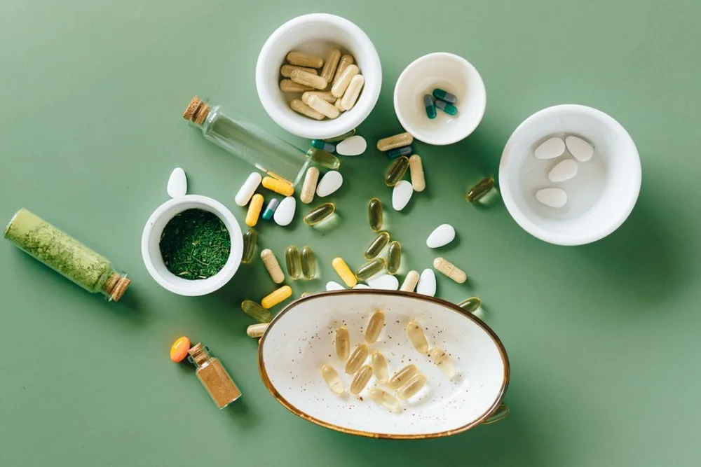 Assorted supplement capsules and tablets arranged in small ceramic bowls on a green surface.