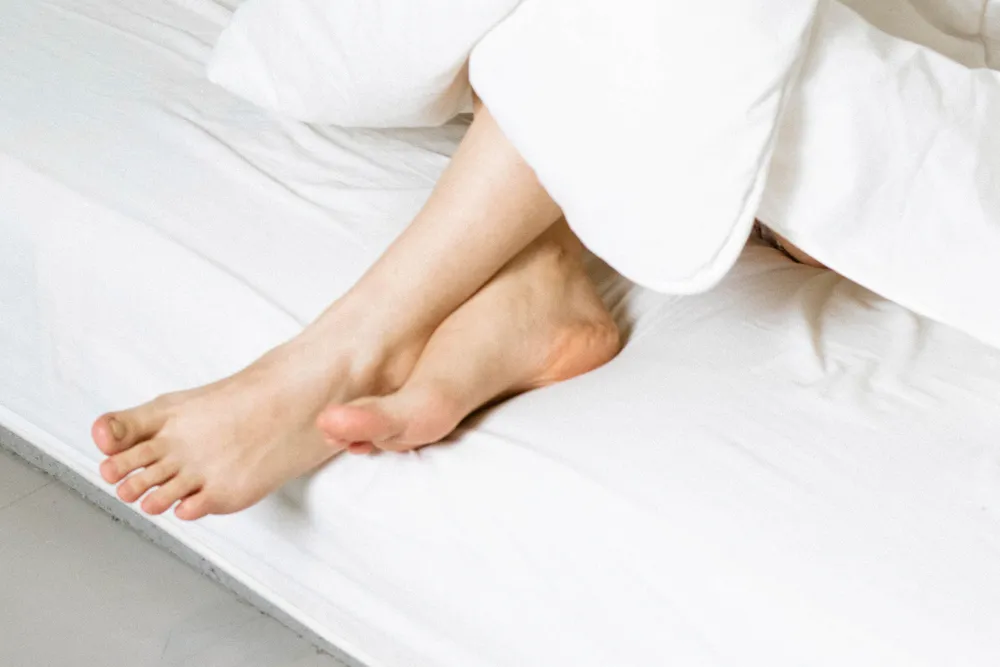 Bare feet resting at the edge of a white duvet on a bed.