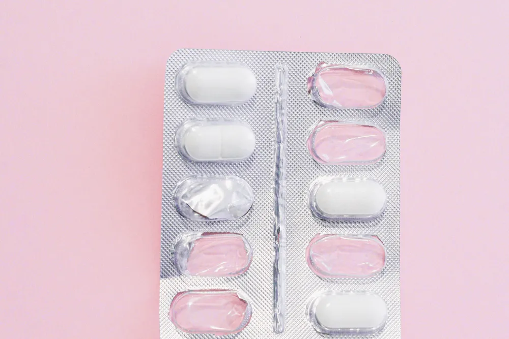 A blister pack of white and pink tablets on a plain pink surface.
