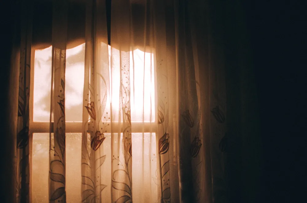 Warm morning sunlight streaming through sheer bedroom curtains.
