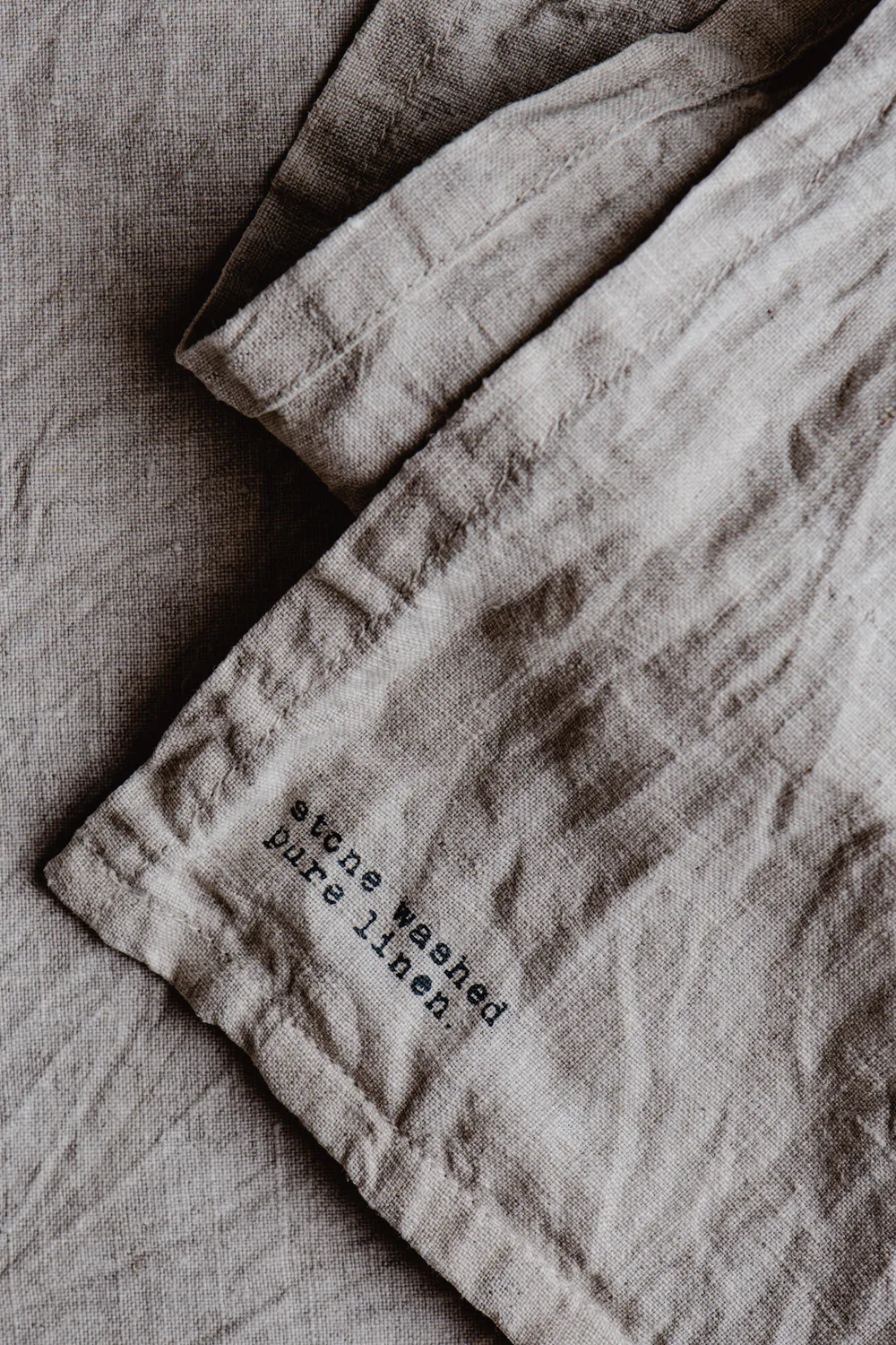 Close-up of stone-washed natural linen fabric with soft folds, labelled pure linen.