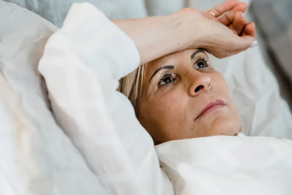 A woman in her late forties lying awake in bed, one hand resting on her forehead.