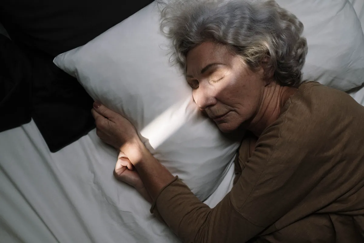 A silver-haired woman in her fifties sleeping peacefully in bed.