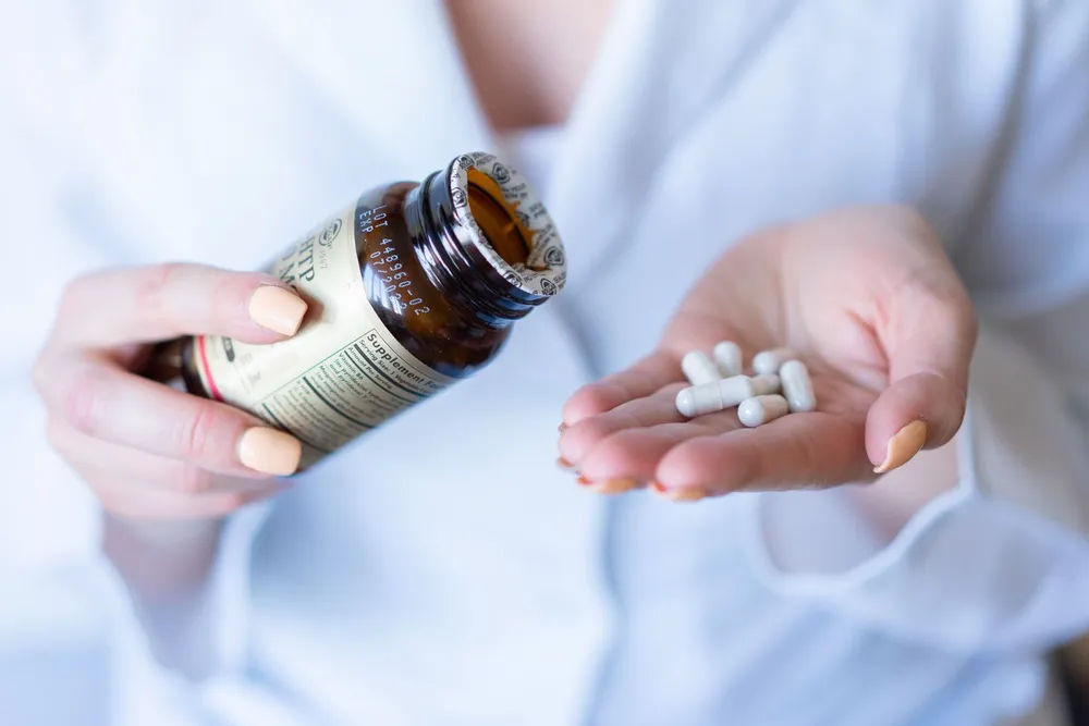 A woman pouring white capsules from an amber supplement bottle into her open hand.