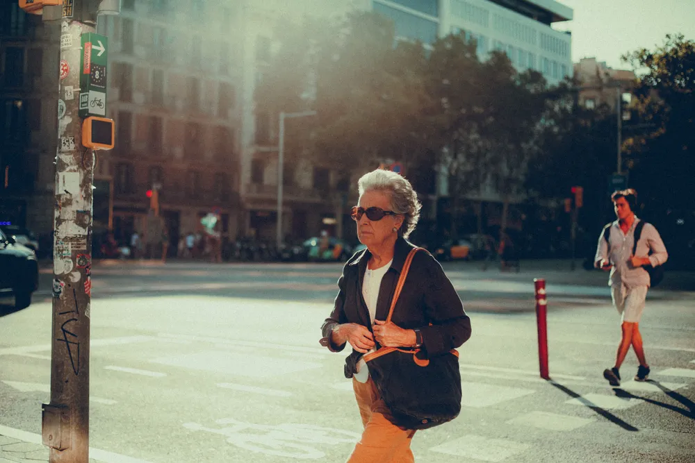 A woman with grey hair walking outdoors in low golden morning sunlight.
