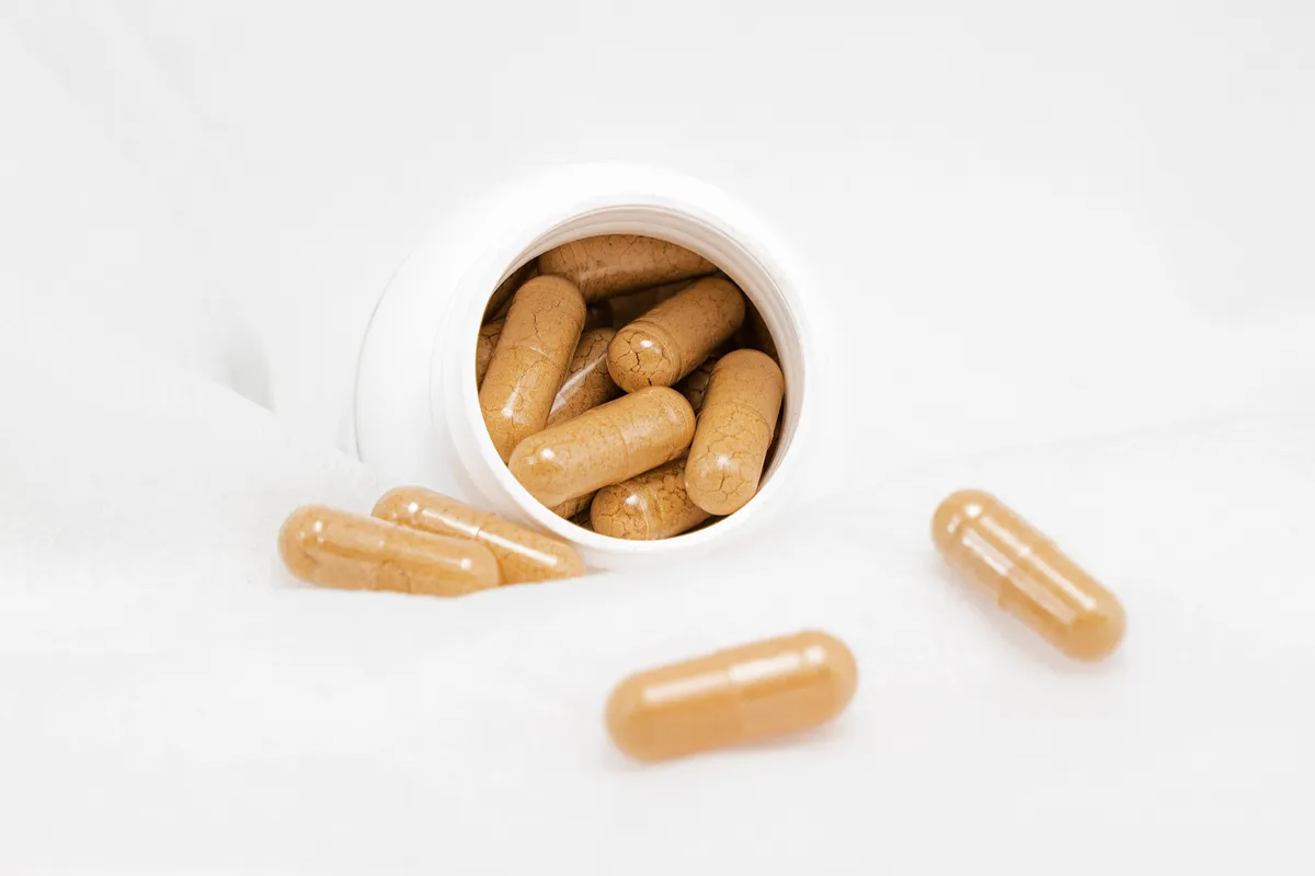 Pale capsules spilling from a small white bottle on a plain background.