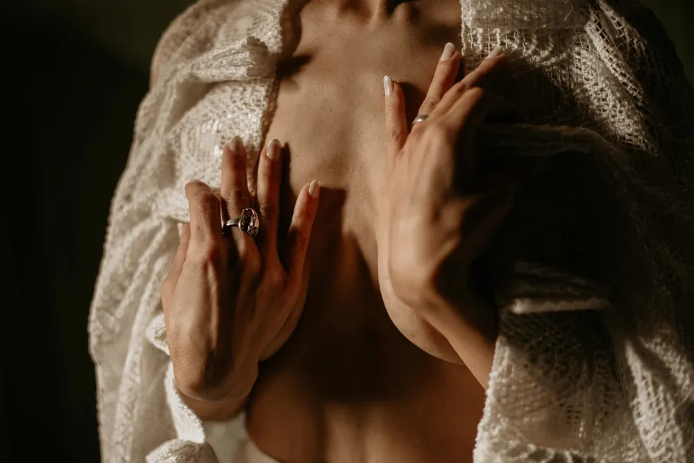 A woman resting her hands gently on her upper chest, in soft warm light.