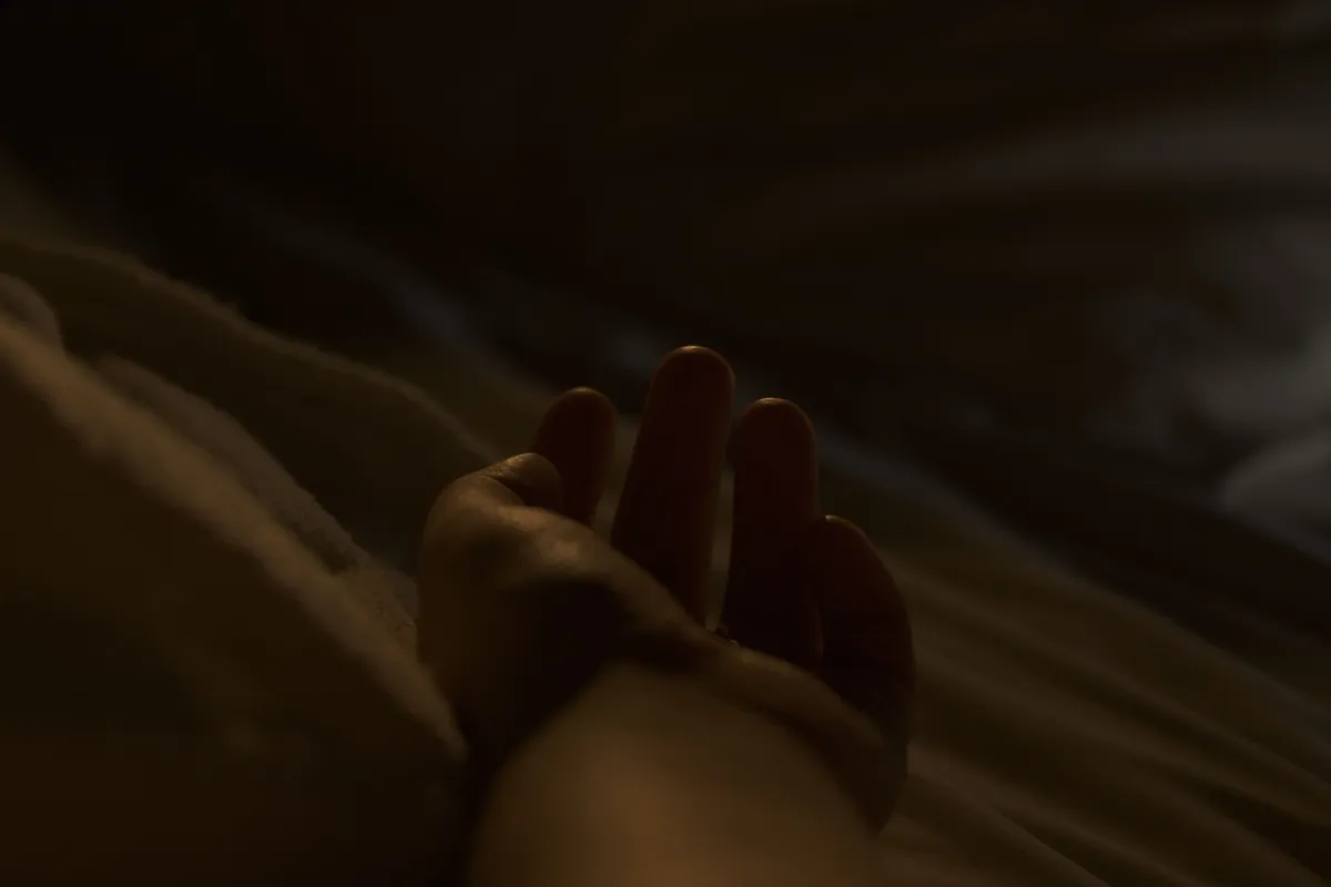 A woman's hand resting on the bedding in a dim bedroom at night.