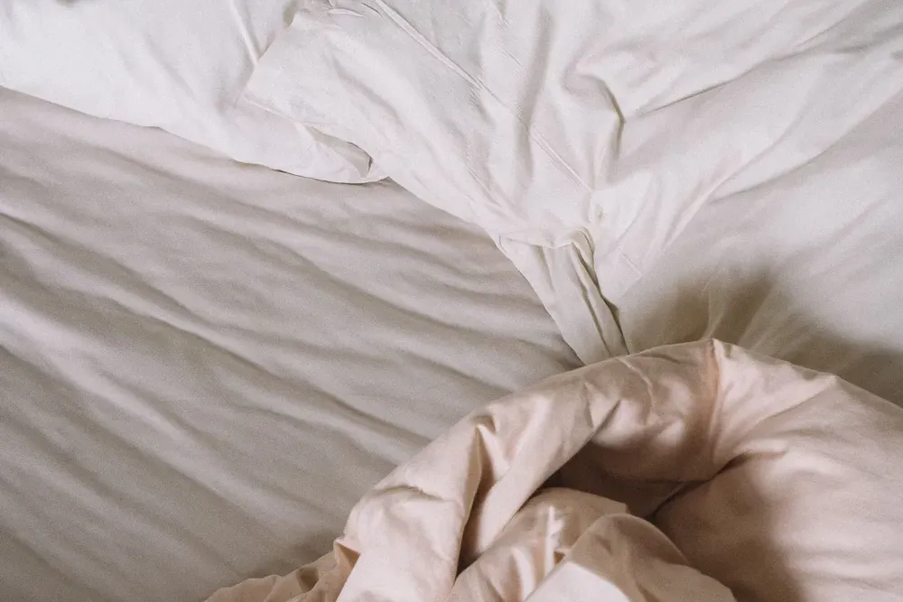 A close-up of a soft white pillow and duvet in natural light.