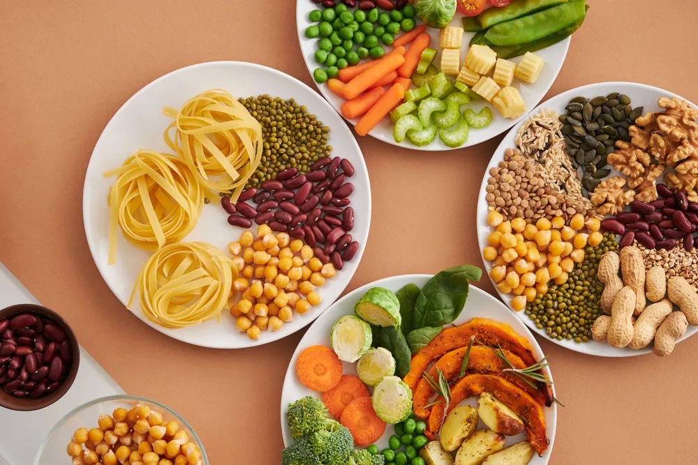 Plates of magnesium-rich foods on a warm background — legumes, chickpeas, pumpkin seeds, nuts, leafy greens and roasted vegetables.