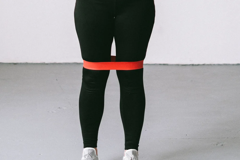 A resistance band looped around the thighs, positioned just above the knees, for a hip-strengthening exercise.