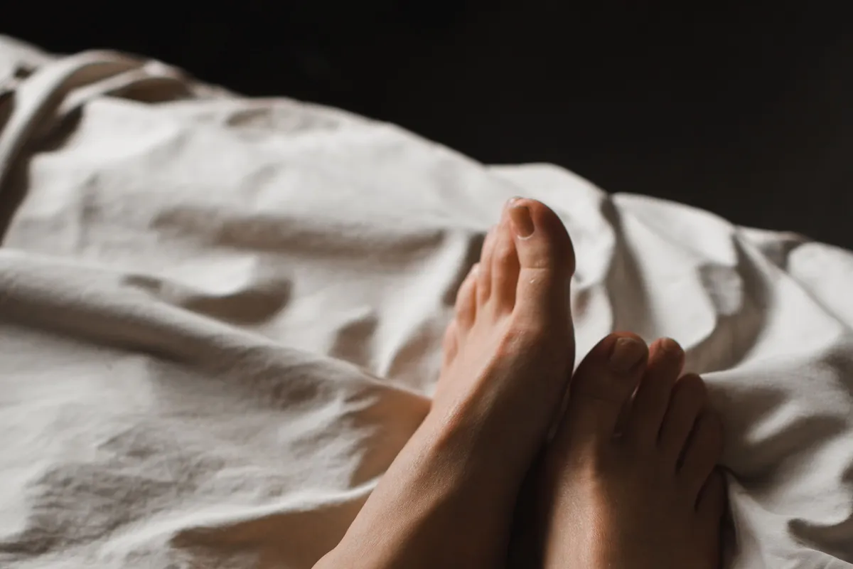Bare feet and lower legs resting on rumpled bedding in a dim bedroom at night.