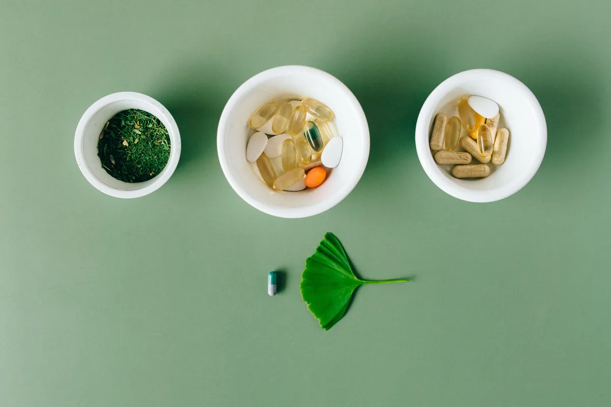 Small bowls of green herb powder and herbal supplement capsules with a ginkgo leaf on a green background.
