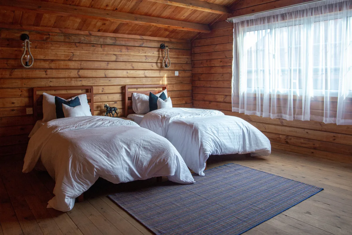 Two single beds side by side with white bedding in a warm wood-panelled bedroom lit by a curtained window.
