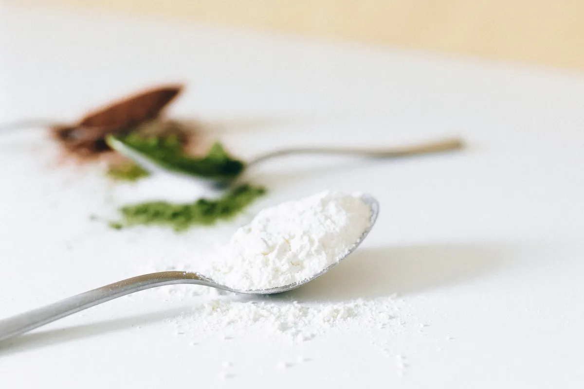A spoon of fine white powder on a pale surface.