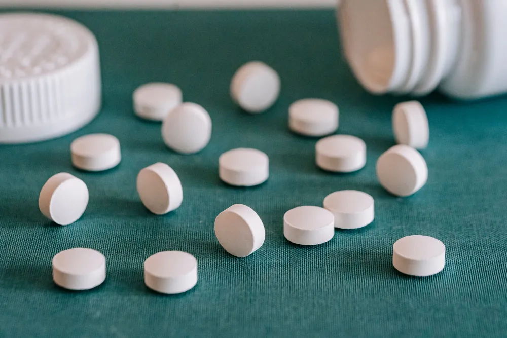 Plain white round tablets scattered on a dark green cloth beside an open white bottle.