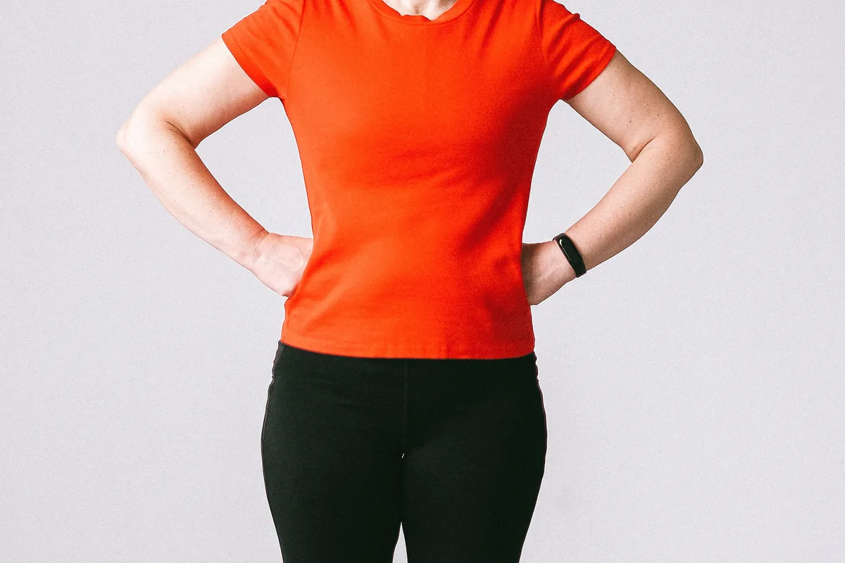 A woman in workout clothes standing with both hands resting on her hips.