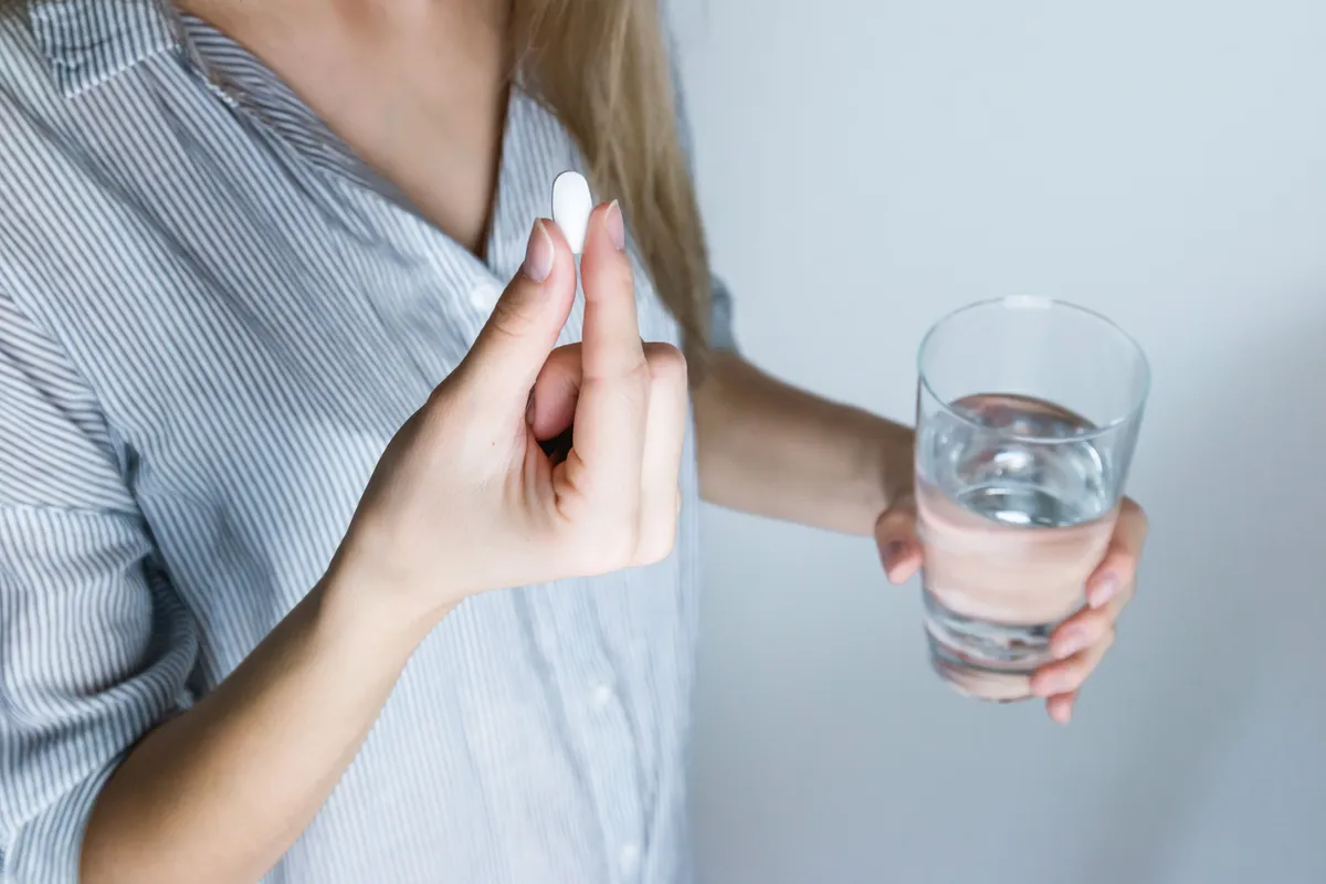 A woman holding a white tablet in one hand and a glass of water in the other.