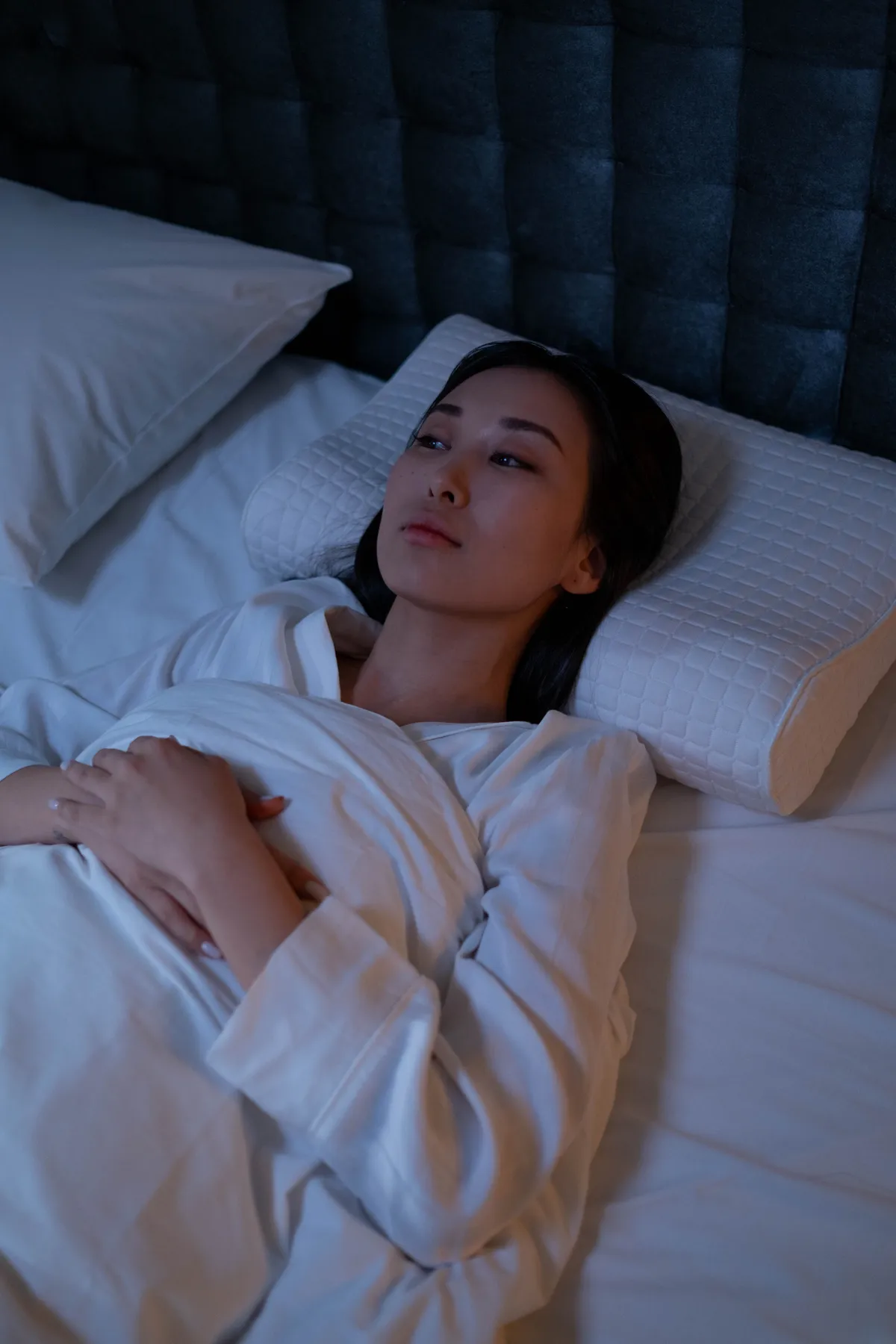 A woman lying awake in bed at night, alert despite being tired.