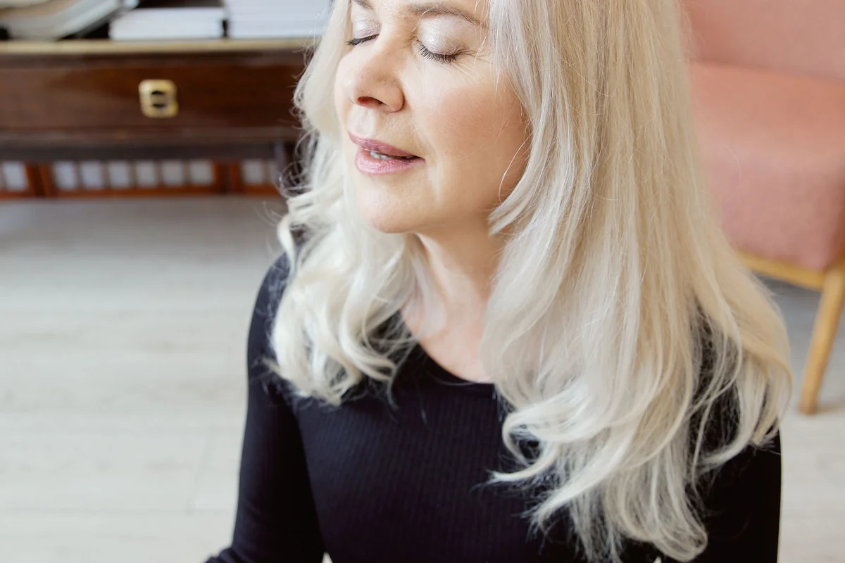 A woman with eyes closed, meditating peacefully in a calm room.