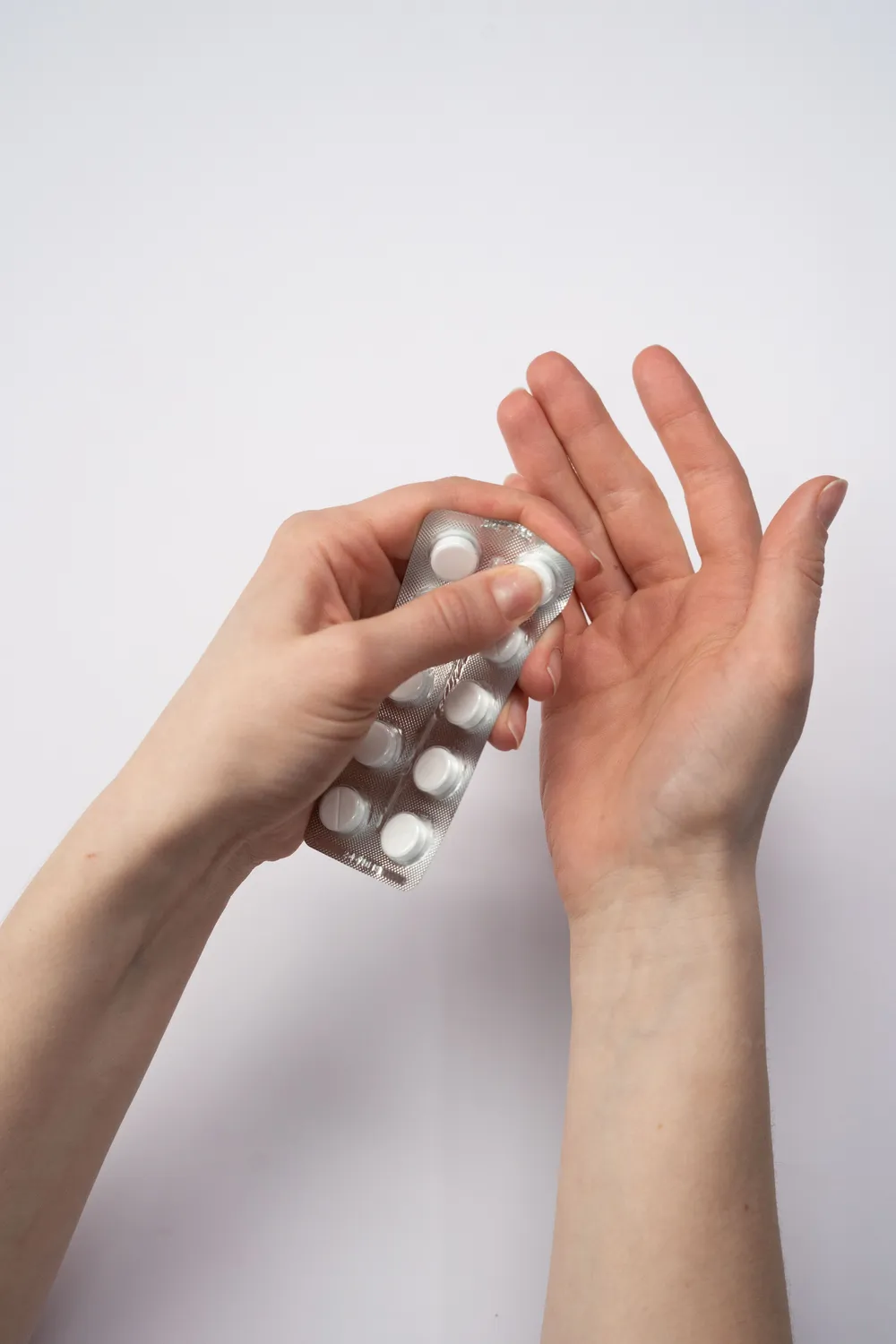 A woman's hands holding a blister pack of tablets against a plain background.