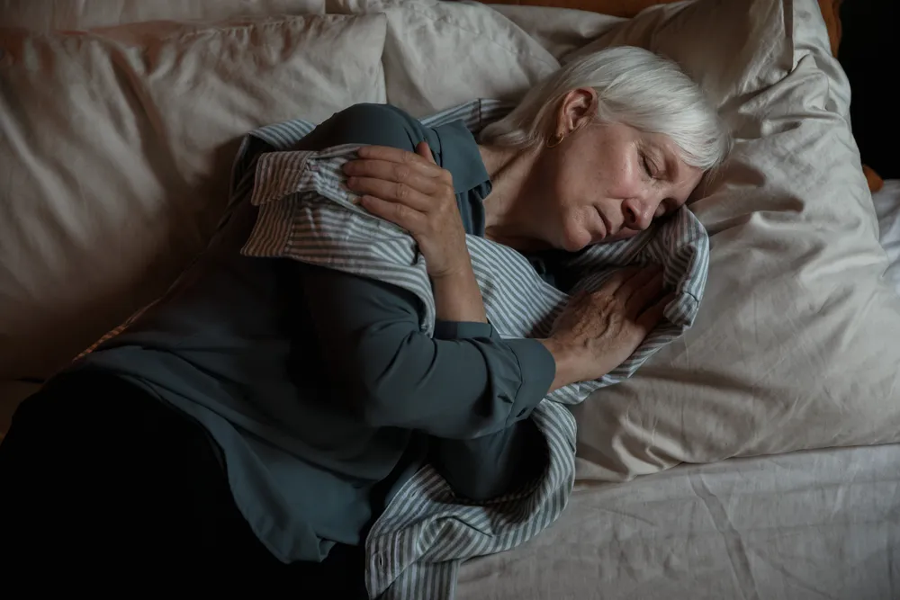 A woman with silver hair sleeping peacefully in bed in soft, warm light.
