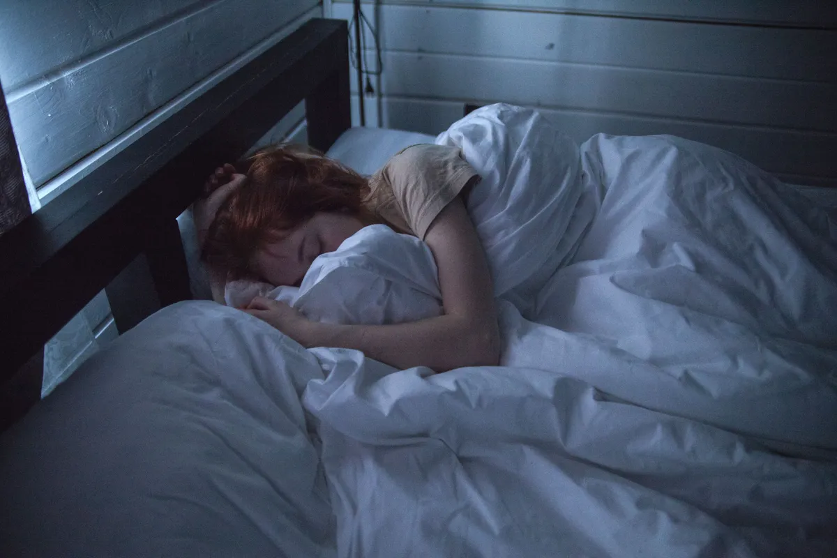 A woman sleeping peacefully in bed at night under soft light.
