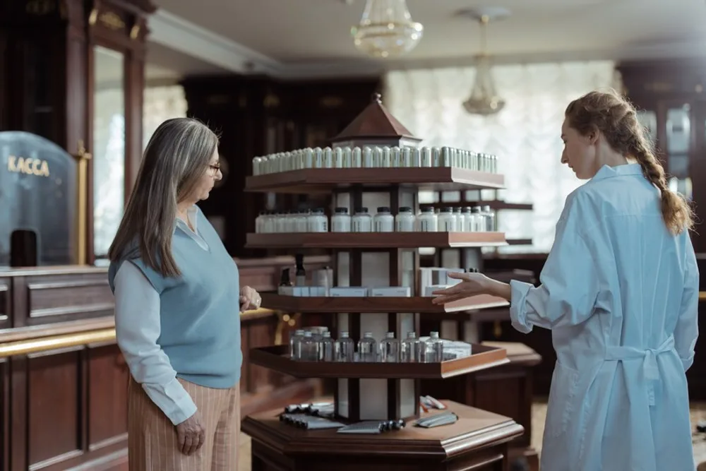 A woman in her fifties talking with a pharmacist beside a display of bottles at a pharmacy counter.