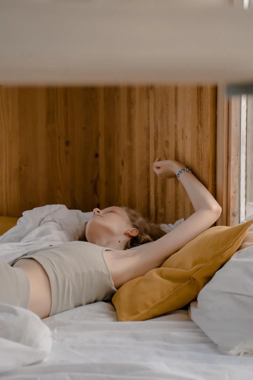 A woman waking and stretching in bed in warm morning light, looking rested.